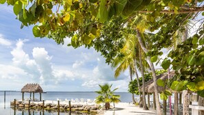 Una playa con una cabaña de techo de paja, palmeras y un mar tranquilo.