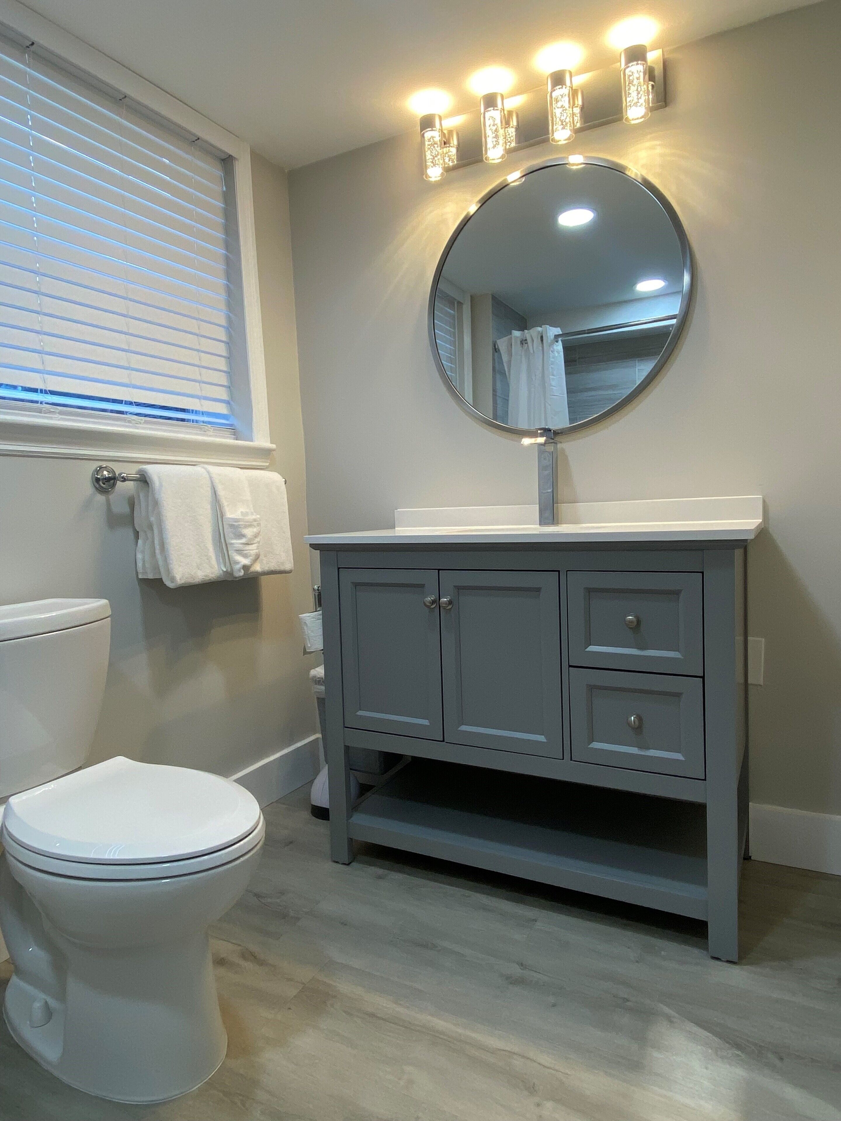 A bathroom with a toilet, vanity, and a mirror with lights above it.