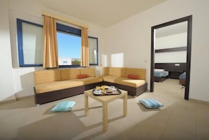 Una sala de estar moderna con un conjunto de sofá, una mesa de centro con alimentos para el desayuno y vistas a través de una ventana con cortinas.