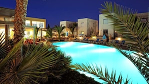 A swimming pool surrounded by palm trees and modern buildings with outdoor seating areas. - Meropi Hotel & Apartments (Hersonissos)