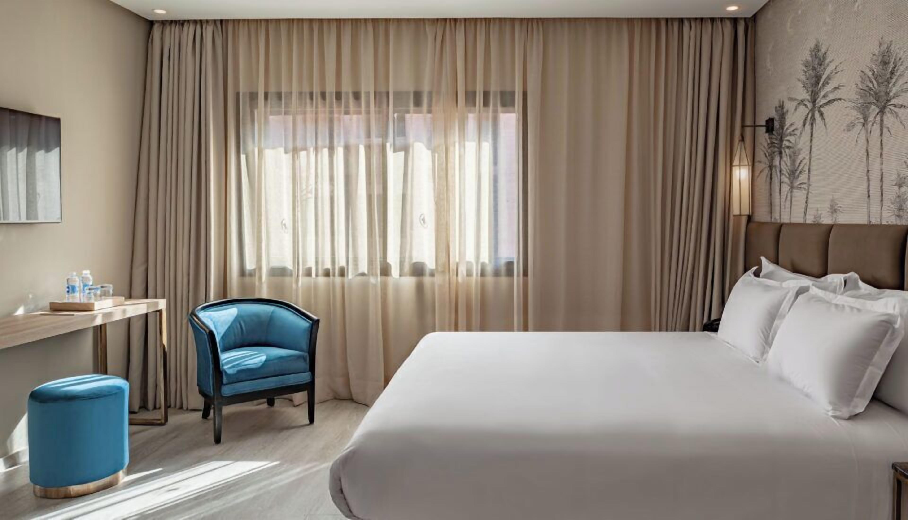 Una habitación de hotel con una cama grande, un escritorio con una silla y una ventana con cortinas.