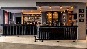 A bar area with two black counters, shelves of liquor bottles, and hanging pendant lights. - Grand Plaza (Marrakech)