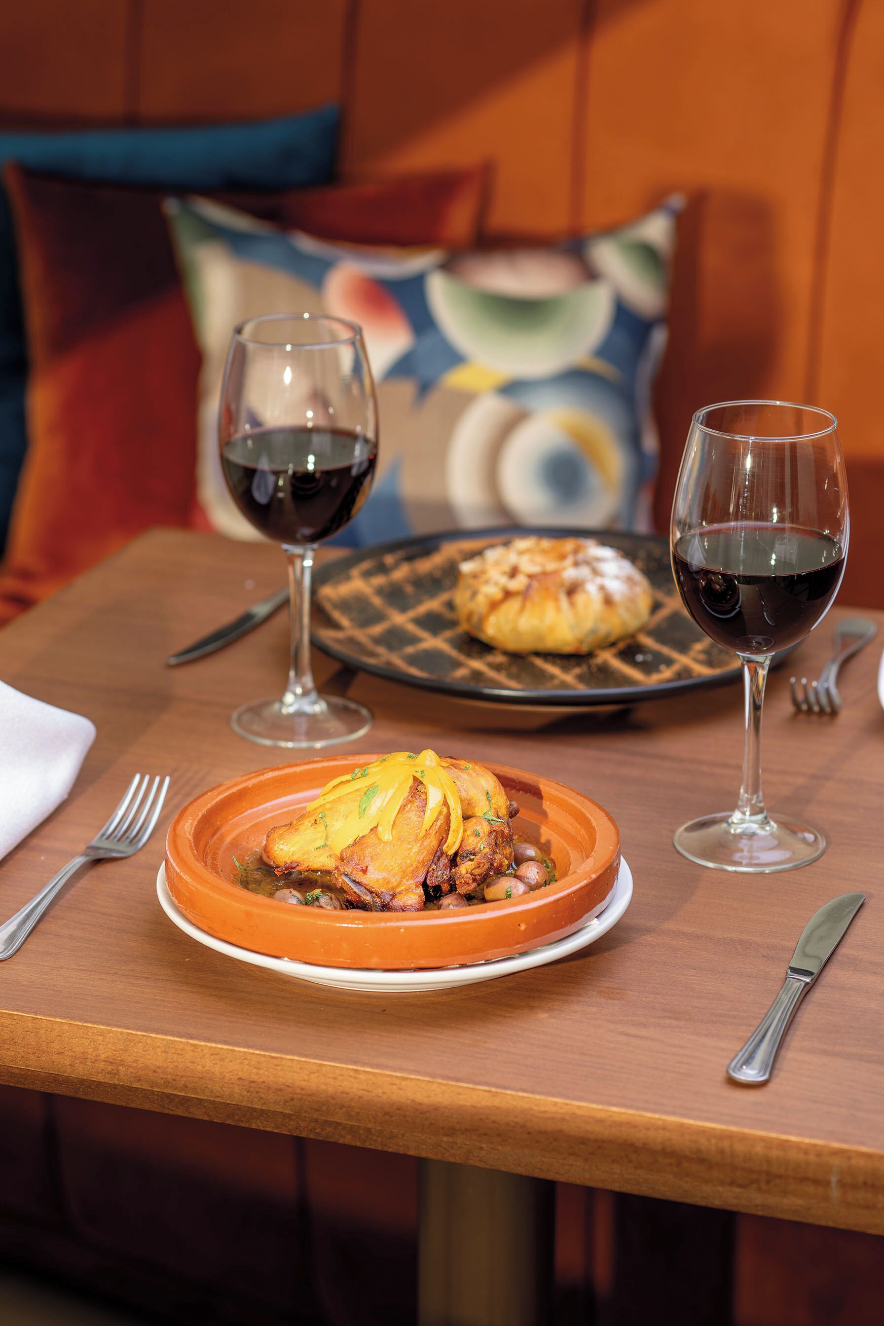 A dining table with a plate of food, two wine glasses, and a fork.
