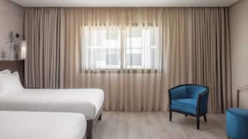 Habitación de hotel con dos camas, un sillón azul y una mesita.