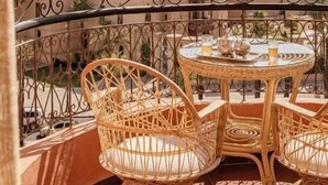 A balcony with wicker chairs and a table, overlooking a cityscape with domed buildings. - Grand Plaza (Marrakech)