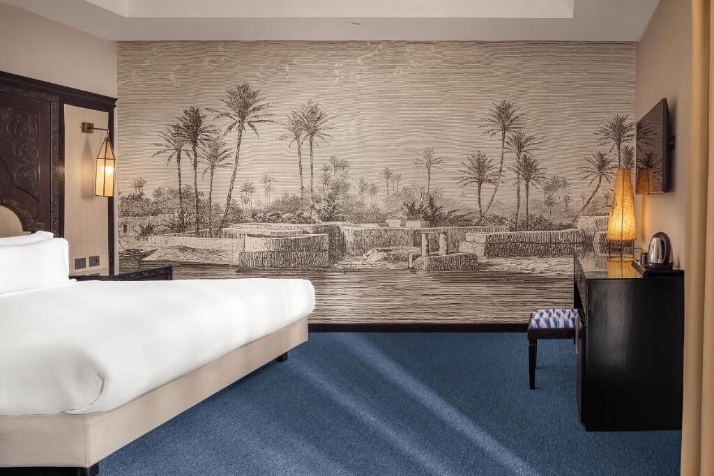 Habitación de hotel con cama, escritorio, silla y un gran mural que representa un paisaje tropical.