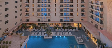 A hotel with multiple balconies, a central swimming pool, and outdoor seating areas.