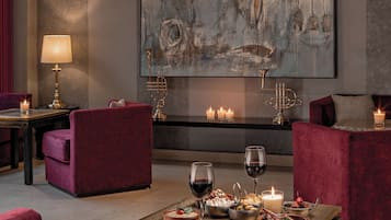 Un salón moderno con asientos cómodos, un cuadro abstracto de gran tamaño, velas y una copa de vino sobre una mesa.