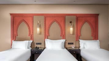 A hotel room with three single beds, each with a wooden nightstand and a lamp.