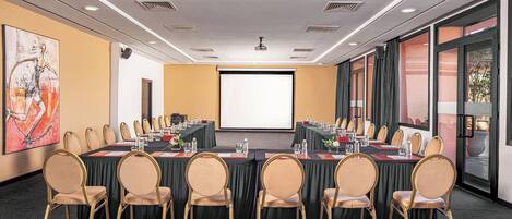 A conference room with a large table, multiple chairs, a projector screen, and a large window with curtains.