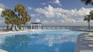Ein Swimmingpool mit Liegestühlen und Palmen, ein überdachter Sitzbereich und Blick auf den Ozean.