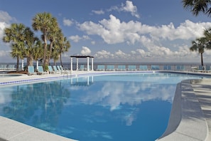 Ein Swimmingpool mit Liegestühlen und Palmen, ein überdachter Sitzbereich und Blick auf den Ozean.