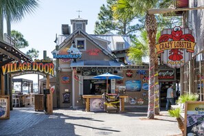 A waterfront restaurant with outdoor seating, a deck side dining area, and a sign for a lobster restaurant. - Bayside at Sandestin (Miramar Beach)