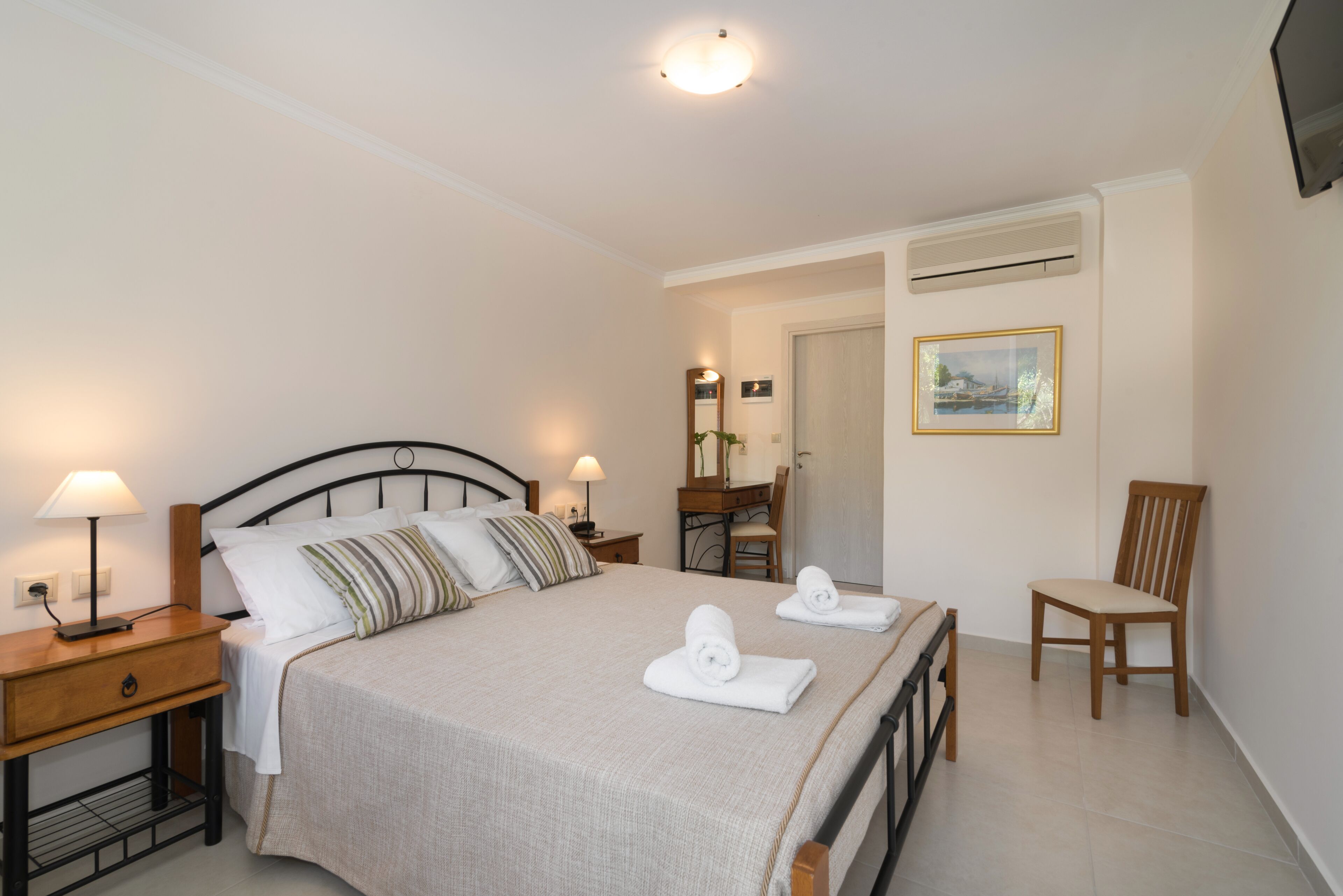 A neatly arranged bedroom with a bed, two bedside tables with lamps, a wooden chair, and a desk with a chair.
