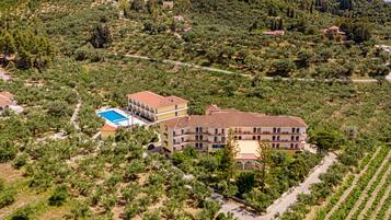 Un hotel grande de varios pisos con tejado de tejas rojas, rodeado de olivares y un paisaje montañoso.