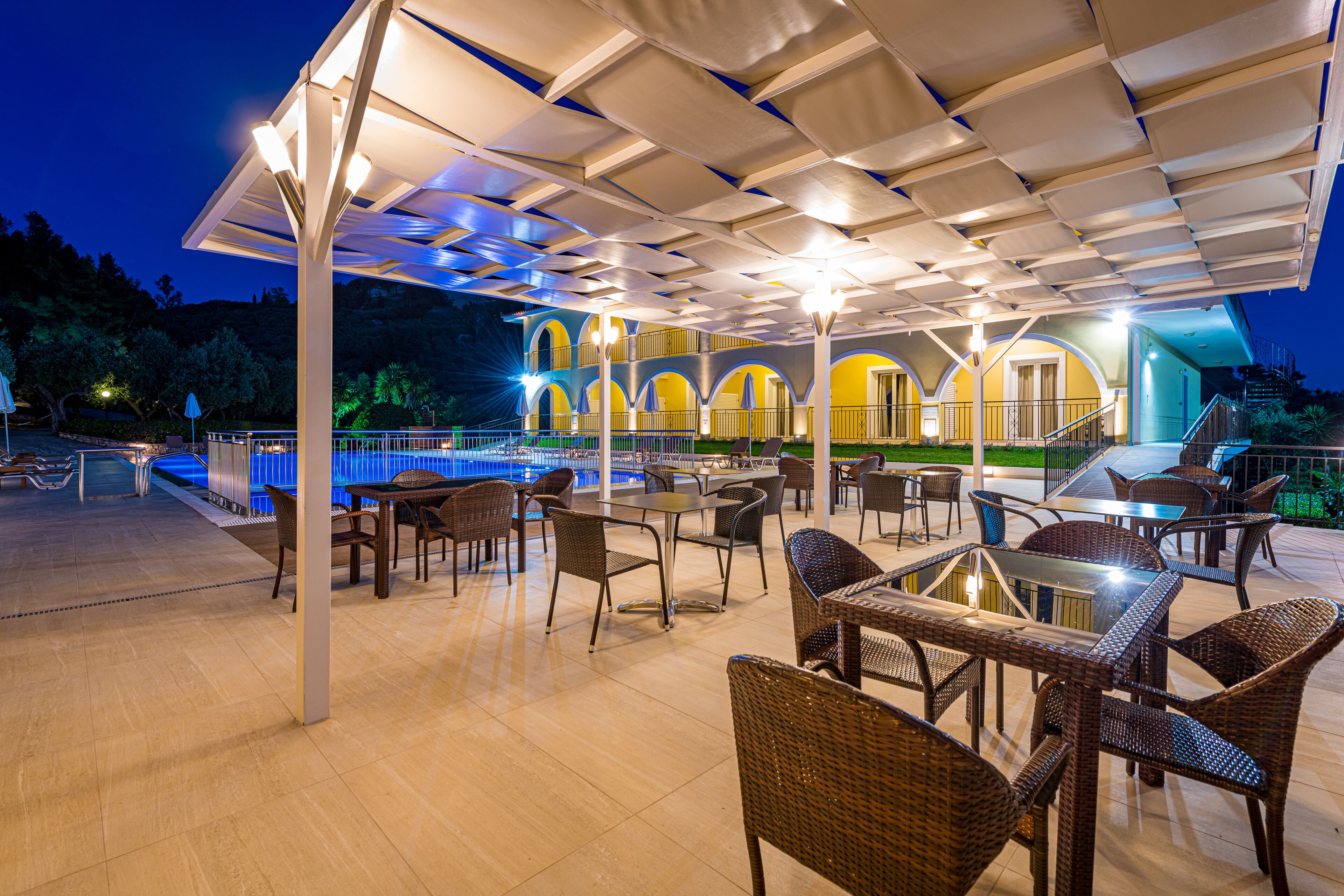 Un patio exterior con mesas y sillas, una piscina y una zona de estar cubierta con vistas a la piscina.