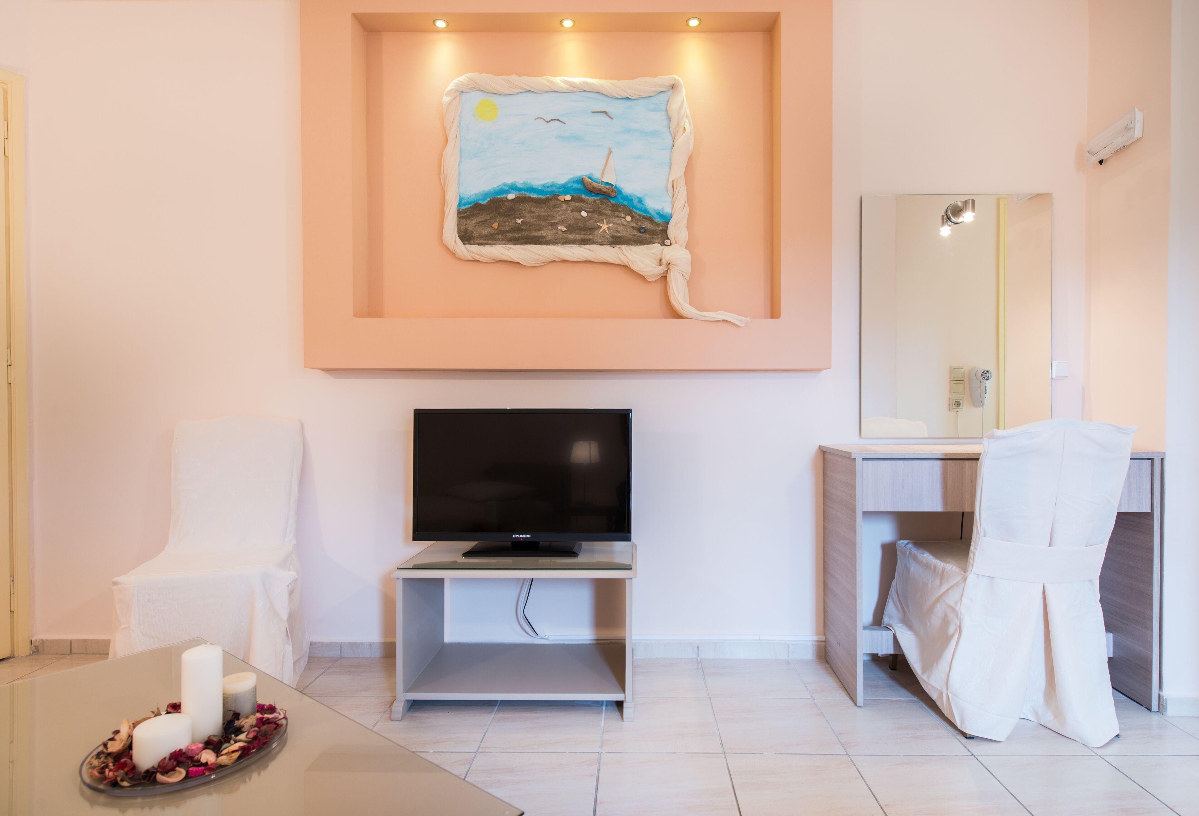Une salle de bain moderne avec un grand miroir, un téléviseur posé sur un meuble, une chaise et un tableau décoratif au mur.