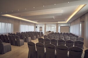 Una sala conferenze con file di sedie, un podio e uno schermo di proiezione.