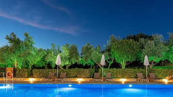 A swimming pool with lounge chairs and umbrellas, surrounded by trees and greenery.