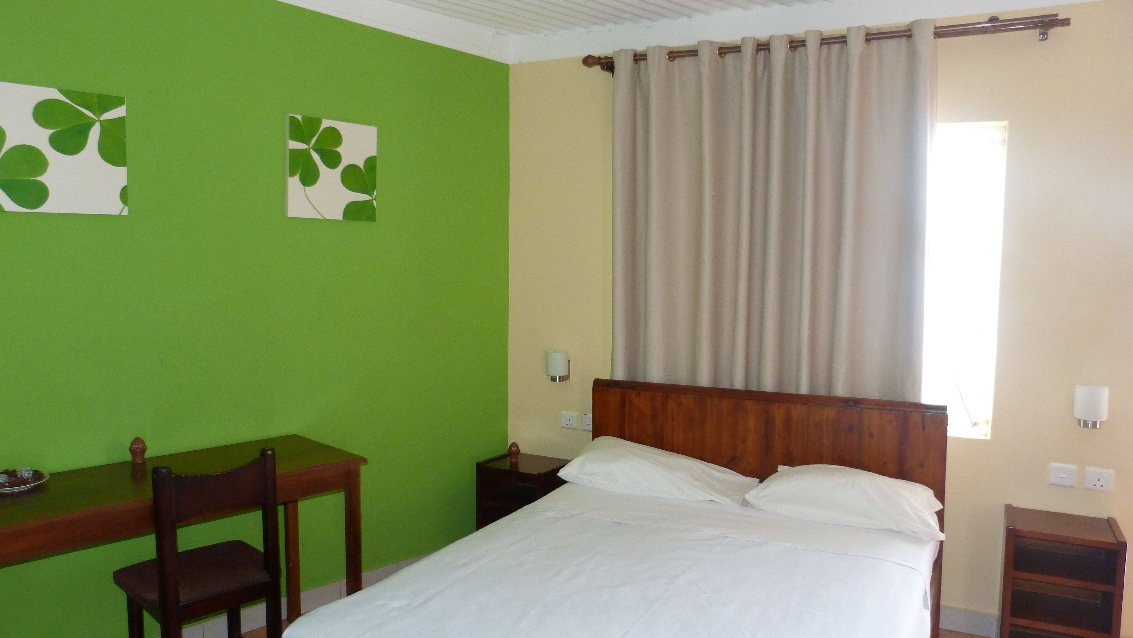 Una habitación con una cama, un escritorio y una silla. Hay dos lámparas fijadas a la pared.