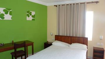 Una habitación con una cama, un escritorio y una silla. Hay dos lámparas fijadas a la pared.