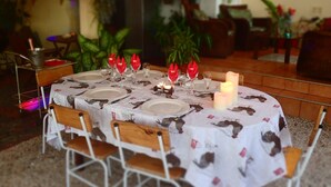 Una mesa redonda para comer dispuesta con platos blancos, servilletas rojas y velas, rodeada de sillas de madera.