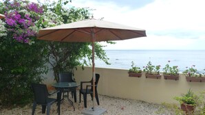 Un patio al aire libre con una mesa y sillas bajo un paraguas grande, con vistas al mar.