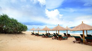 Une plage bordée de rangées de chaises longues et d’ombrelles en chaume, un rivage sablonneux et l’océan en toile de fond.