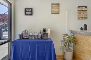 Una habitació amb una taula coberta per un mantell blau, una màquina de cafè i diversos recipients. Hi ha cartells motivacionals a la paret i una planta en test.