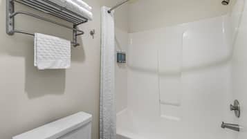 A bathroom with a toilet, a towel rack with folded towels, a shower curtain, and a showerhead.