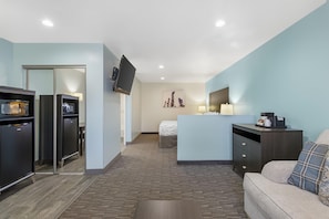 A compact hotel room with a kitchenette, a bed, a sofa, and a flat-screen TV mounted on the wall. - SureStay by Best Western Yerington (Yerington)