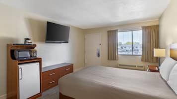 A hotel room with a bed, a television mounted on the wall, a minibar, a desk, and a window with curtains.