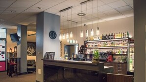 A bar area with a counter, hanging lights, and shelves of bottles. - Economy Silesian Hotel (Katowice)