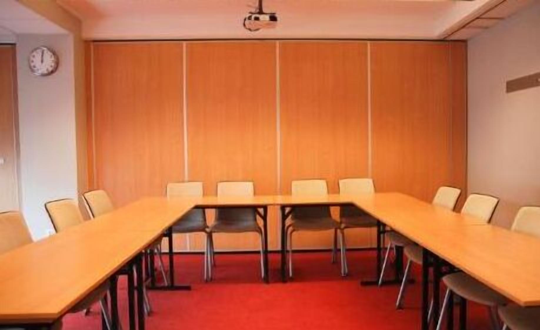 Una sala de conferències amb una taula llarga i cadires, un rellotge a la paret i un projector al sostre.