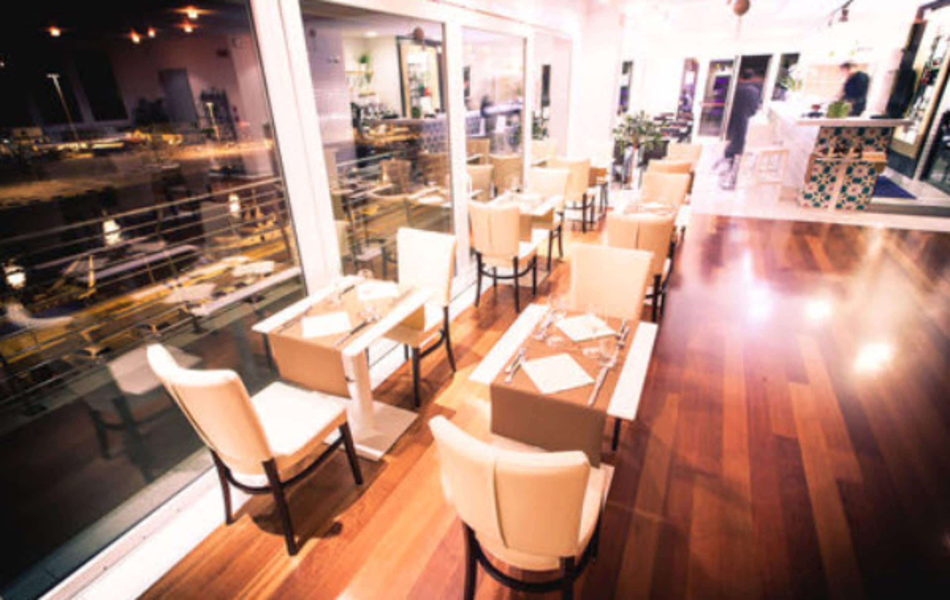 A restaurant with wooden flooring, white chairs, and tables.