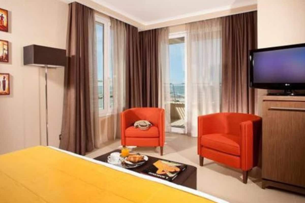 A hotel room with a bed, two red armchairs, a television, and a breakfast tray on the floor.