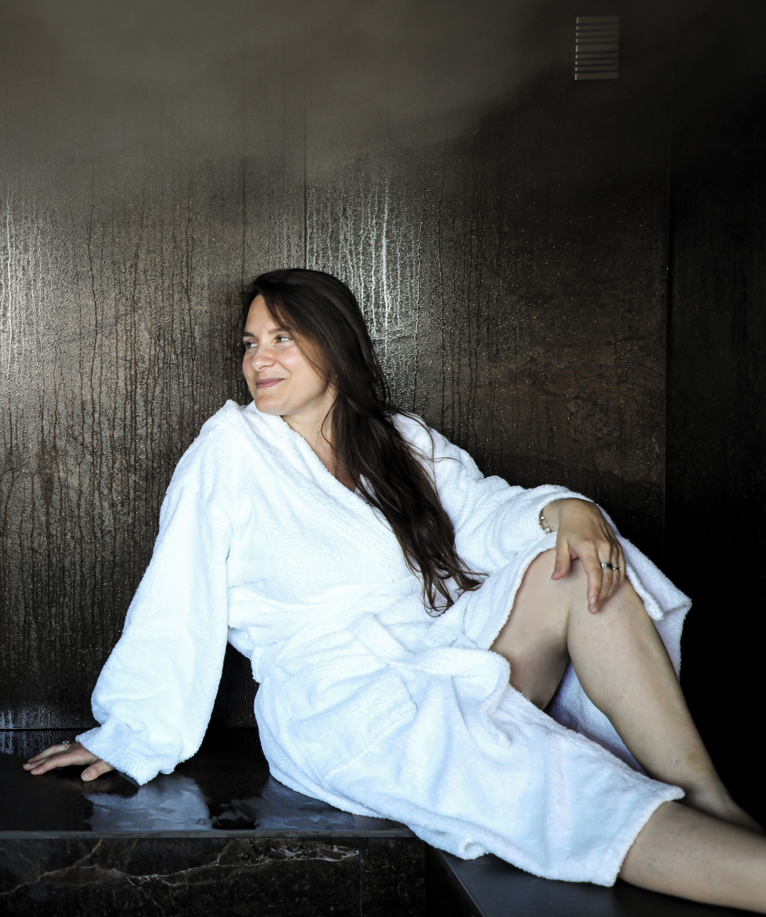 A person sitting in a dimly lit room with a textured wall.