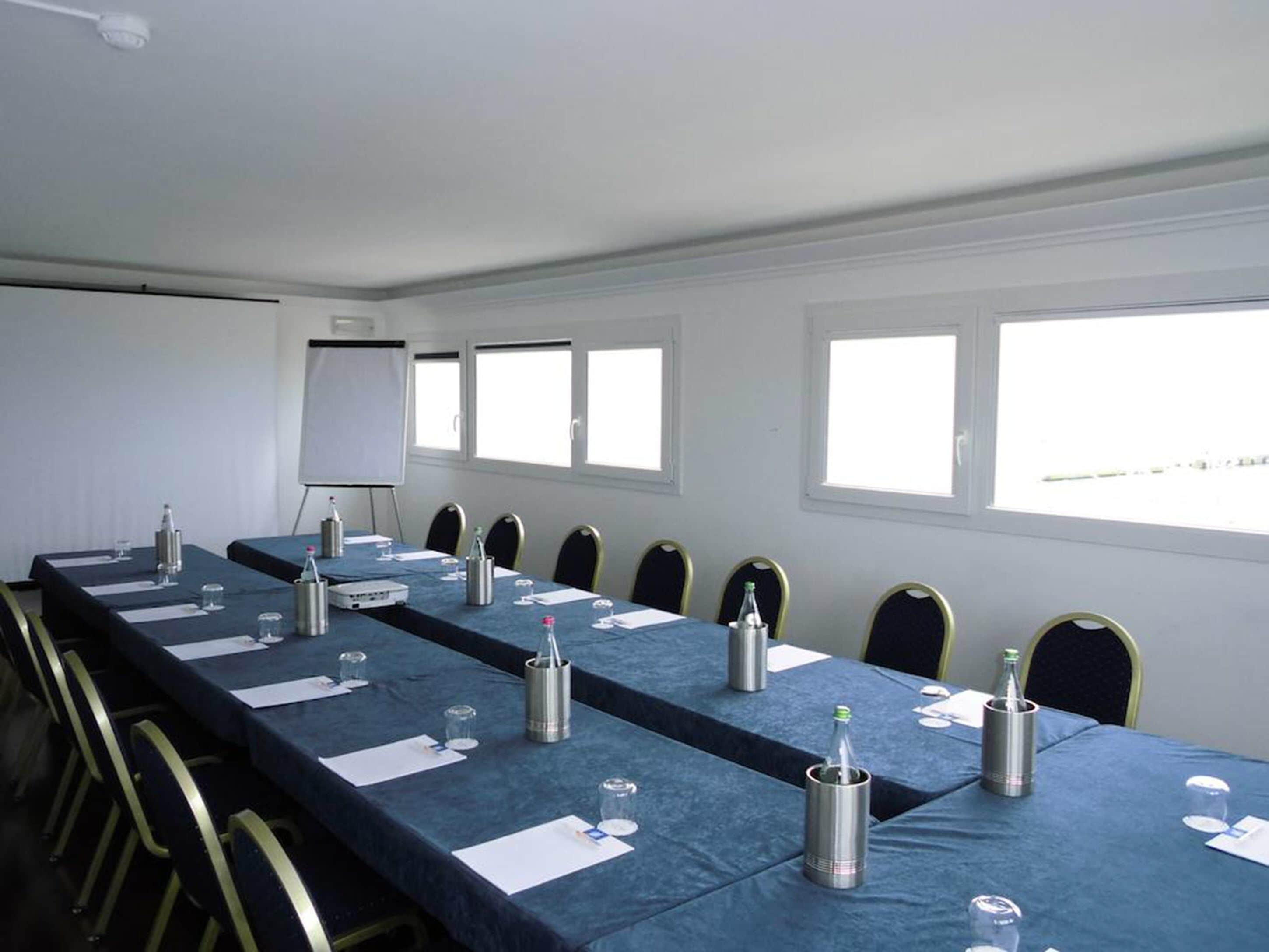Ein Konferenzraum mit einem langen Tisch, Stühlen, einer Wandtafel und Fenstern.