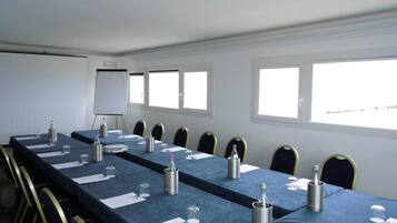 Une salle de conférence avec une longue table, des chaises, un tableau blanc et des fenêtres.