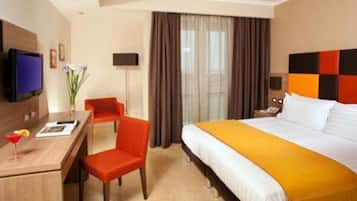 Une chambre d’hôtel avec un lit, un bureau, une chaise, une télévision et une fenêtre avec des rideaux.