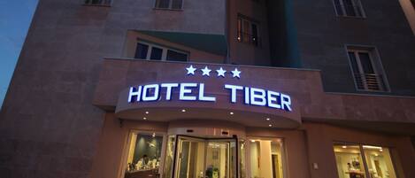 A hotel named "HOTEL TIBER" with a modern facade and illuminated signage.
