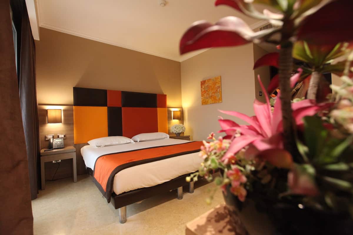 A hotel room with a bed, bedside tables, a wall-mounted TV, and a potted plant.