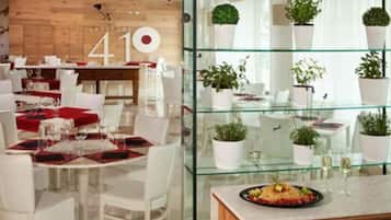 Un comedor moderno con mesas redondas, sillas blancas y detalles en rojo. Hay una vitrina de vidrio con plantas en macetas.