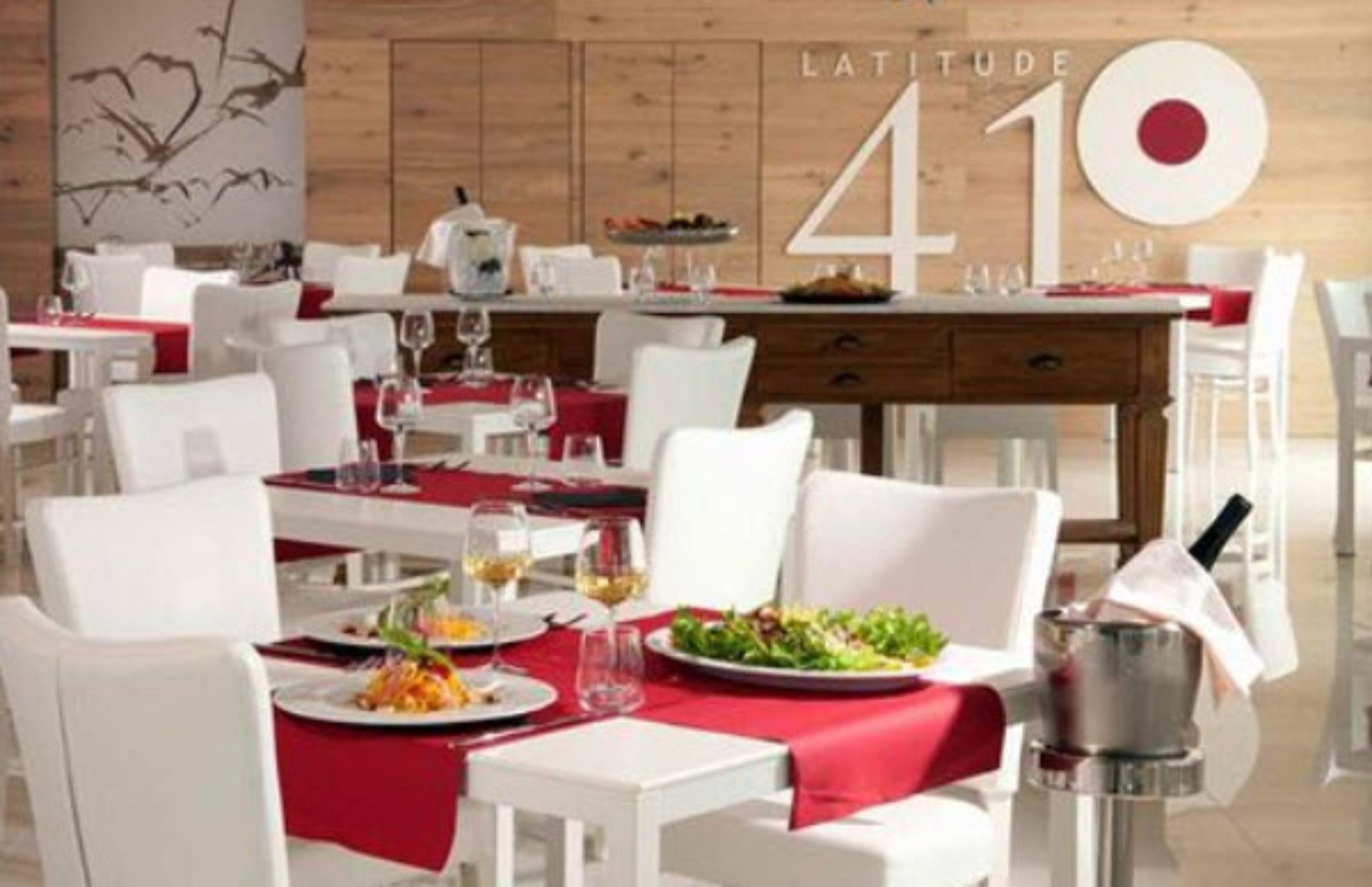 Un restaurant avec des chaises blanches et des nappes rouges, un mur en bois et un grand panneau portant le numéro « 410 ».