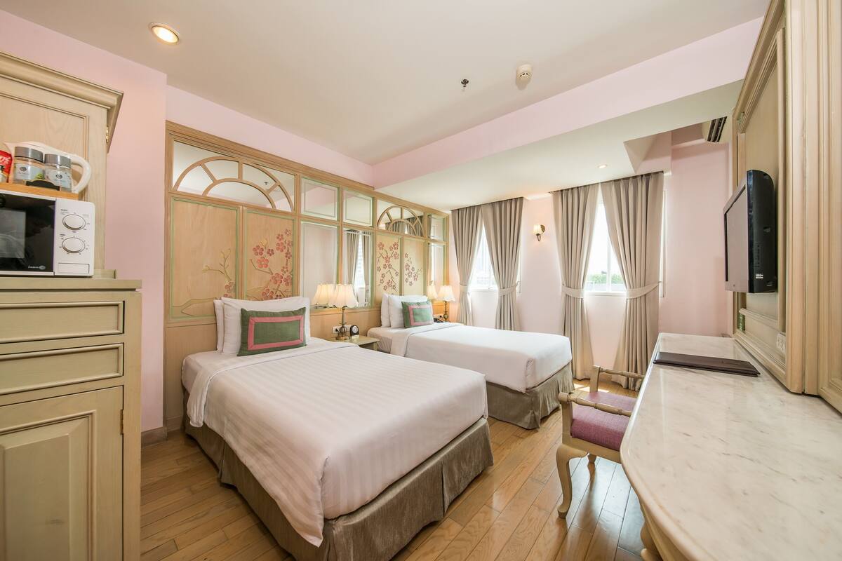 A hotel room with two beds, a television, a desk, and a mirror.