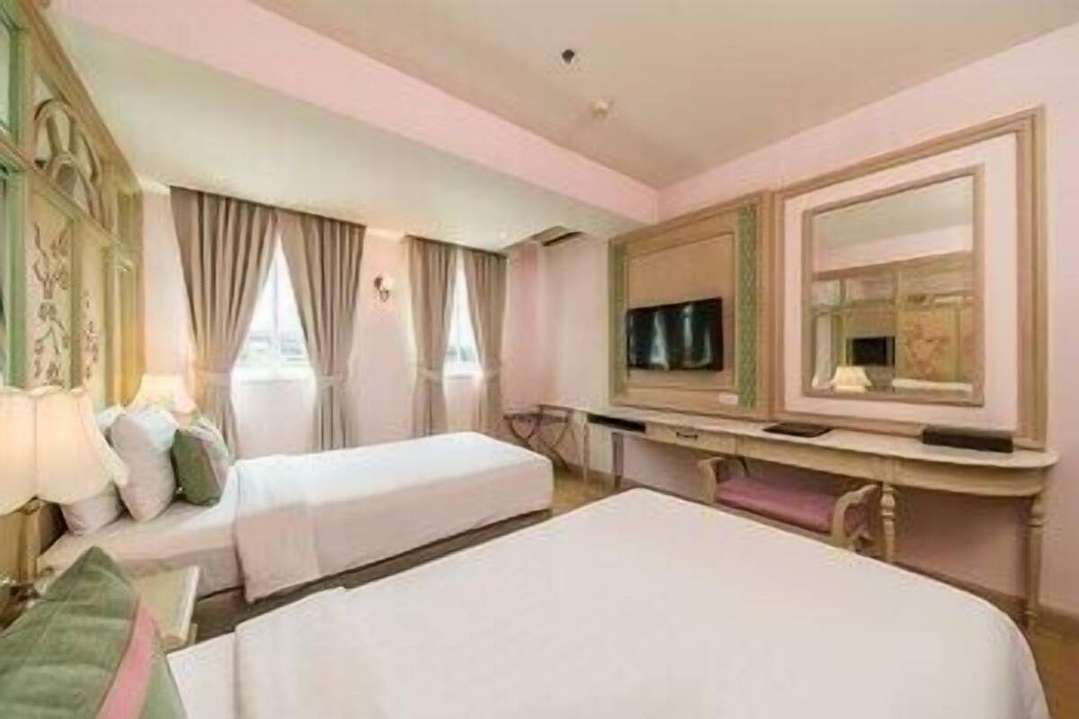 A hotel room with two beds, a desk with a television, and a large mirror.