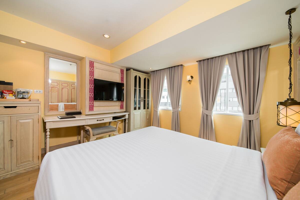 A hotel room with a bed, a desk with a computer, a TV, and a wardrobe.