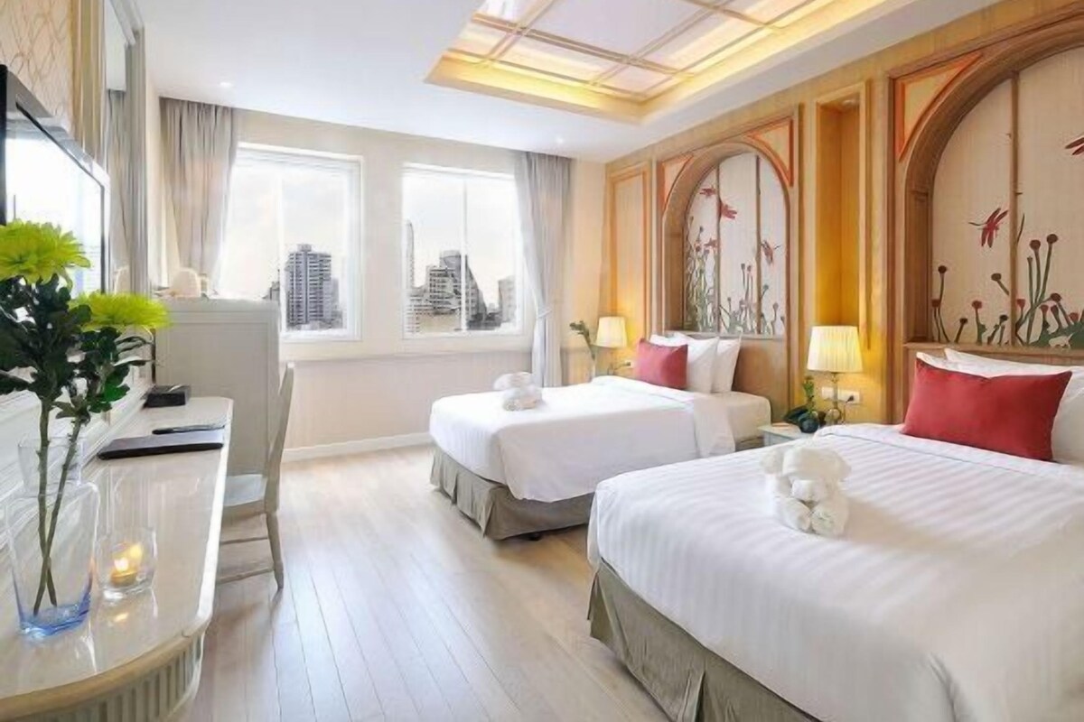 A hotel room with two beds, a desk, and a view of the city.