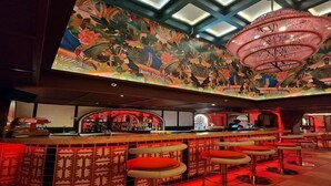 Un espacio de bar con techo alto, un mural grande y varios taburetes.