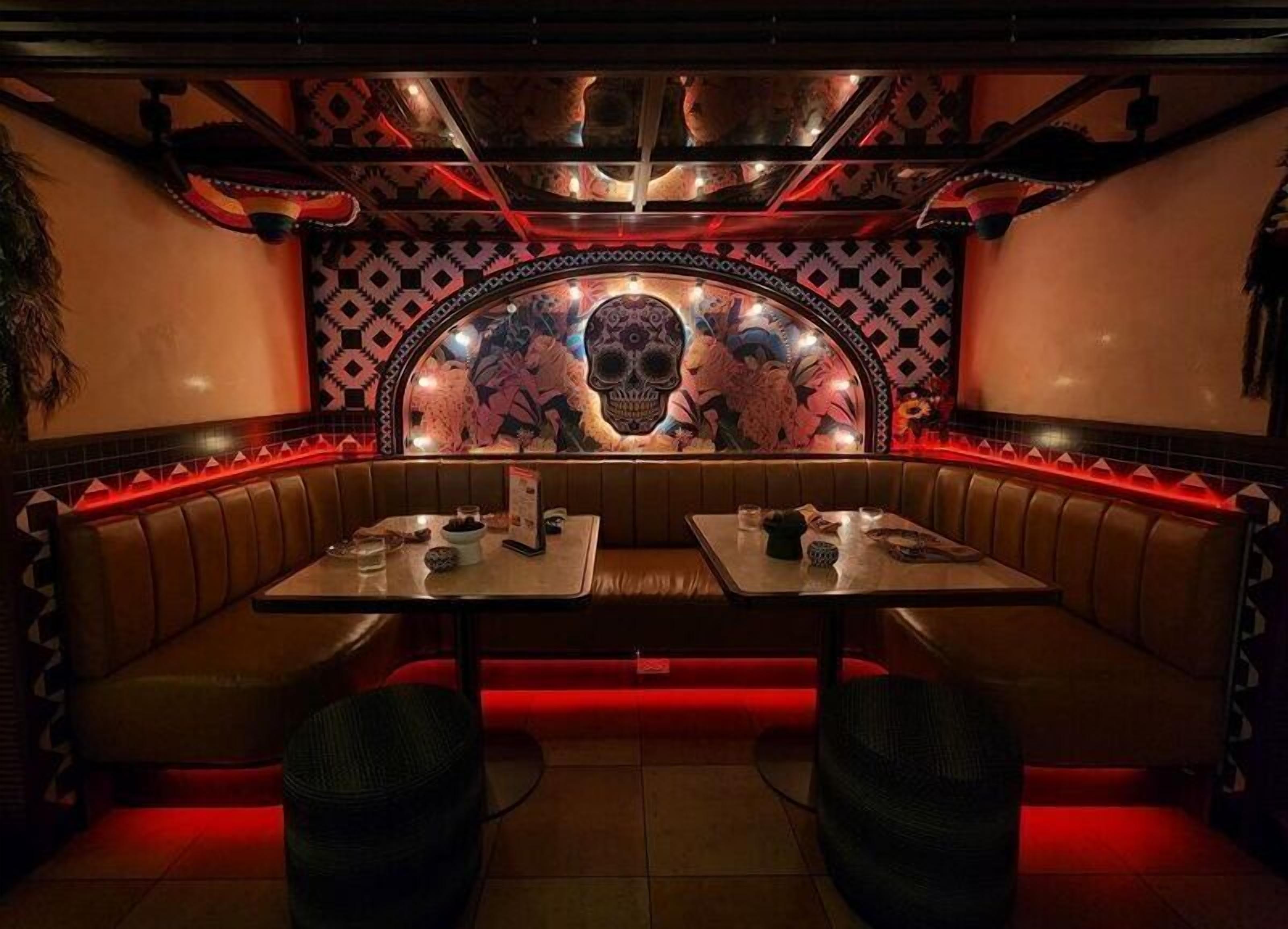 A restaurant with a booth seating area, a skull mural on the wall, and red ambient lighting.